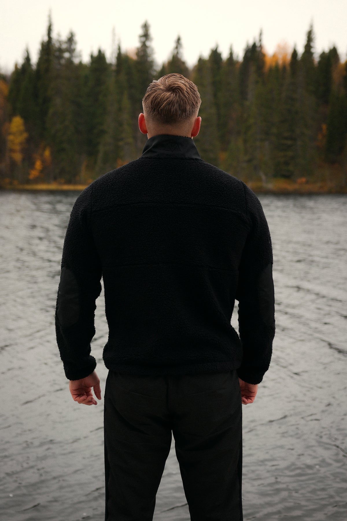 Black teddy fleece jacket with smooth shoulder panels and elbow patches worn outdoors