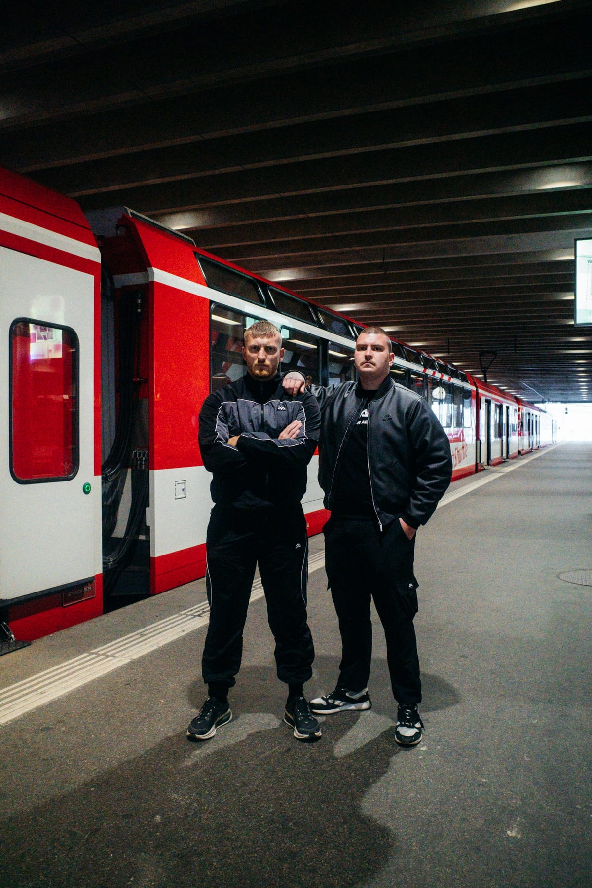 Mann in schwarzer Trackjacke und passender Hose auf einem Bahnsteig