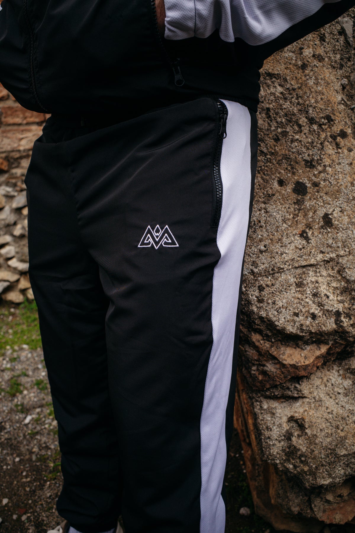 Vorderansicht: Schwarze Trackpants mit weißem Seitenstreifen und gesticktem Logo