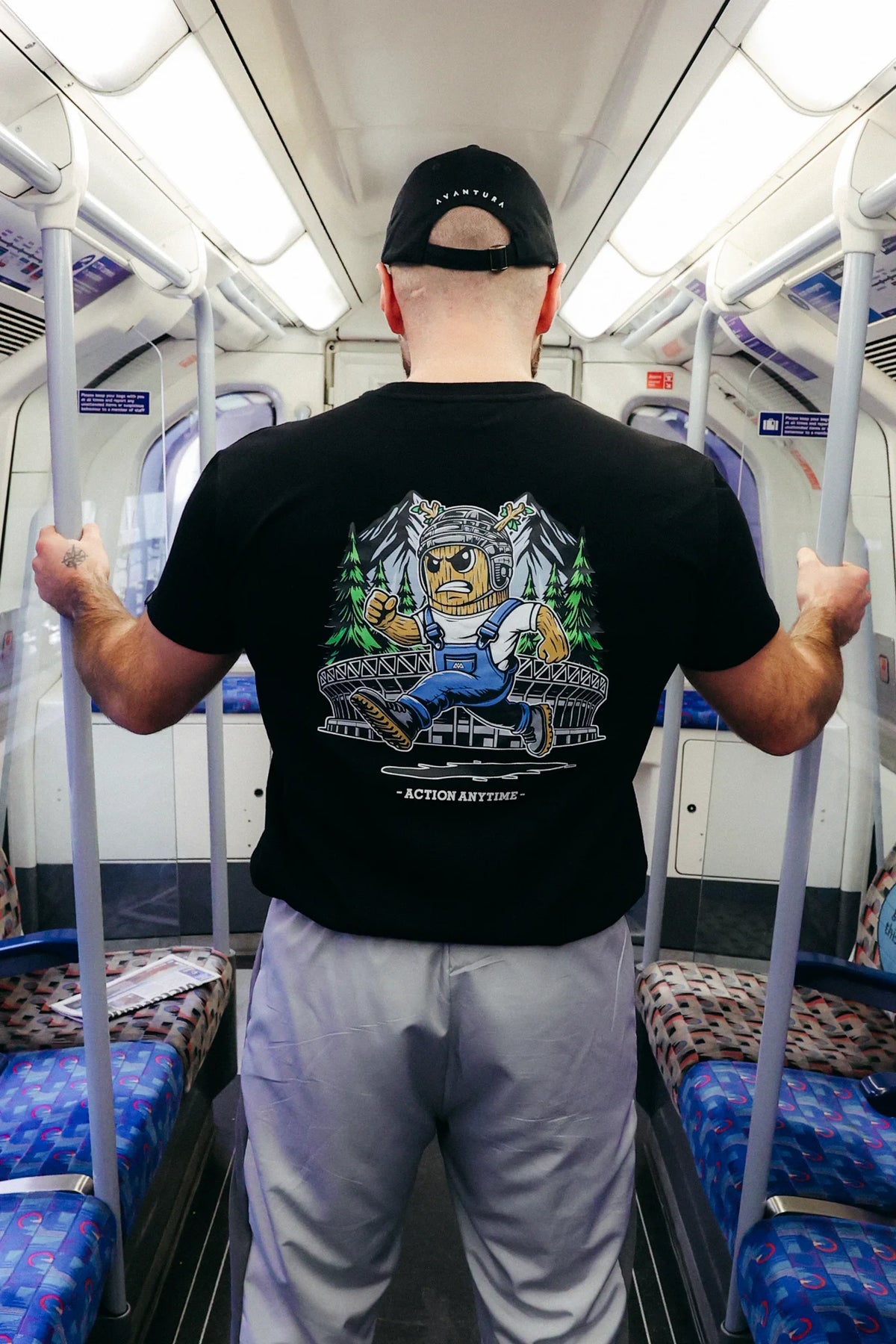 Man holding train rail wearing black T-shirt with large back print of running tree character