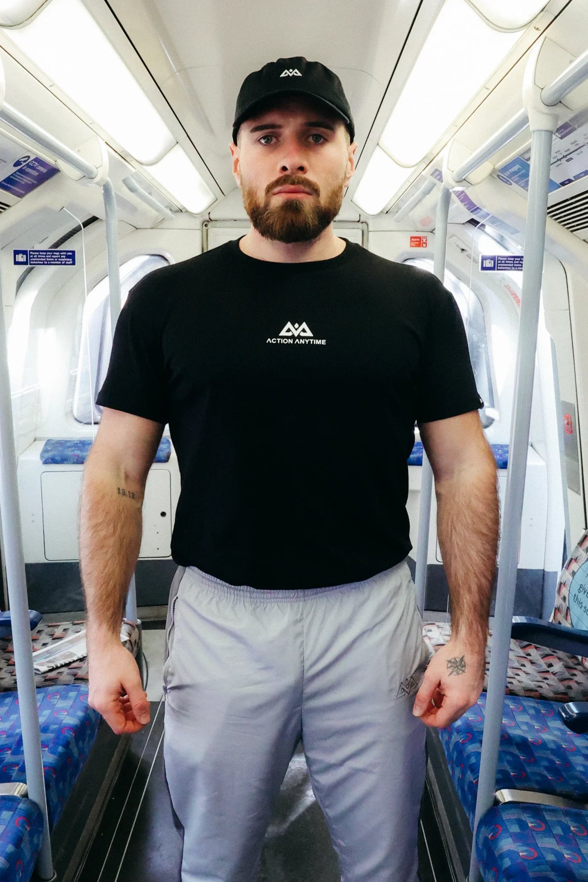 Black Avantura T-shirt with white Action Anytime chest logo worn by man on train
