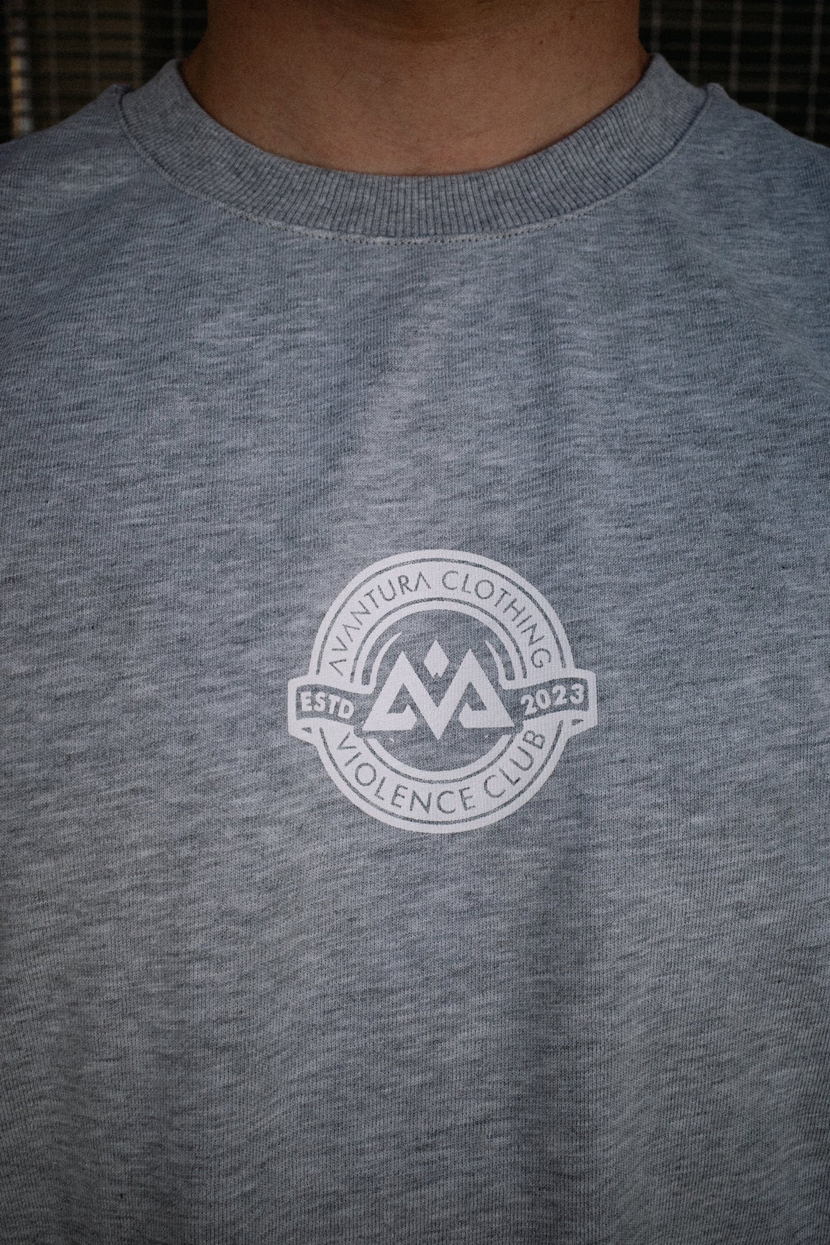 Close-up of heather grey t-shirt chest featuring white screen-printed AVANTURA CLOTHING logo