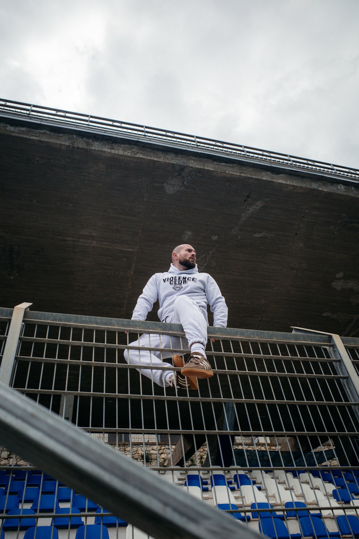 Full body shot of man in light grey heathered sweat suit sitting on railing